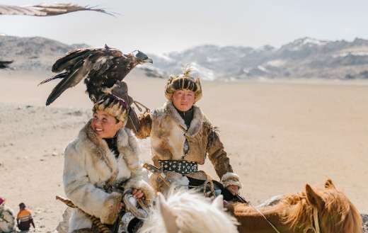 Positive Mongolian eagle hunters riding horses on mountainous terrain