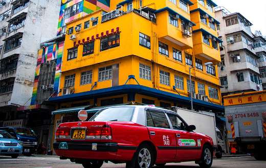 Red taxi passing classic yellow old building Hongkong