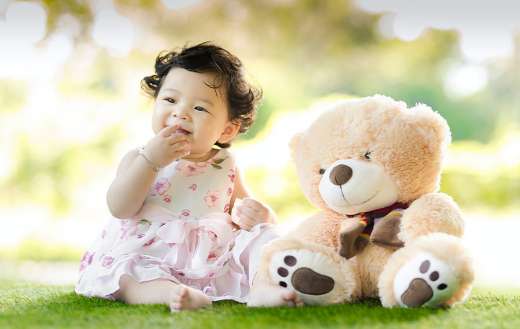 Baby sitting on grass beside bear toy puzzle
